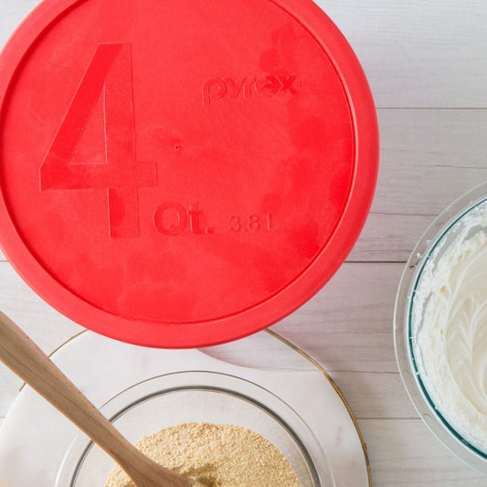 Pyrex measuring cup lid with a wooden spoon and ingredients on a white surface