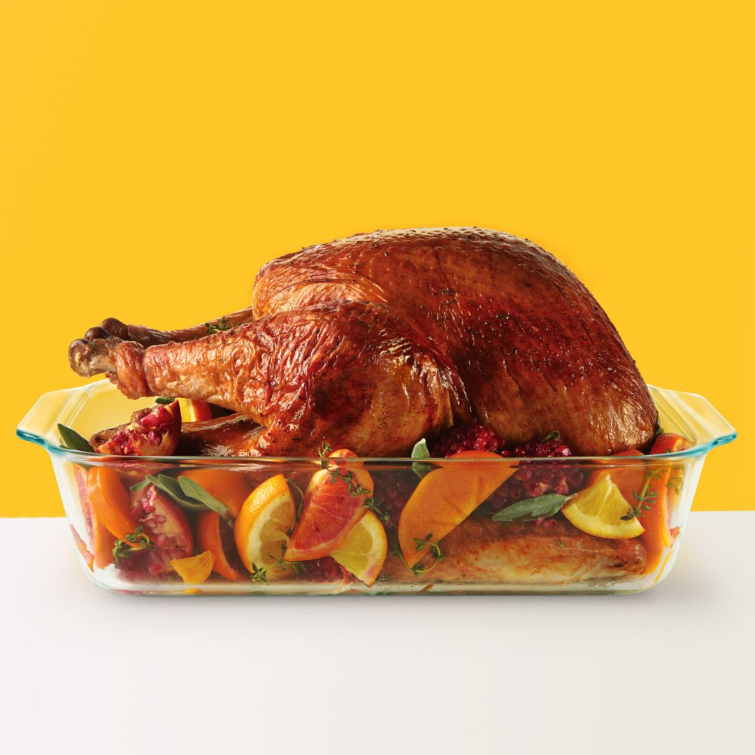Roasted turkey in a glass dish with fruits and herbs on a yellow background